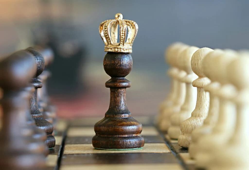 Close-up of a chess pawn wearing a crown, facing down the opposing pawns